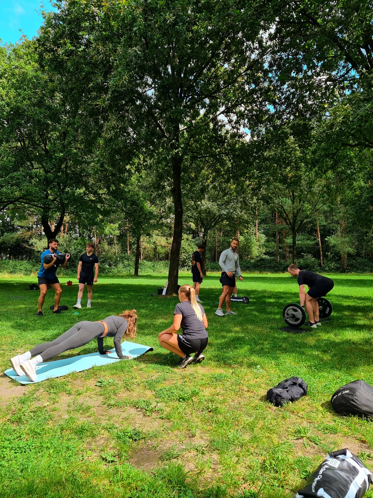 Deelnemers doen planken, squats en deadlifts tijdens een bootcampsessie van Het Krachtkantoor in de buitenlucht